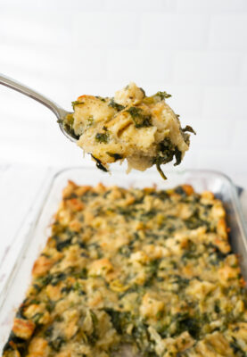 Spoonful of Spinach Artichoke Bread Pudding in casserole dish.