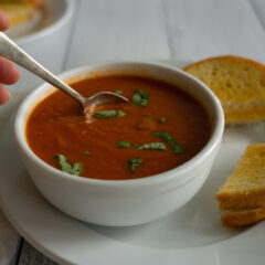 Slow Cooker Tomato Basil Soup in a white bowl with spoon and grilled cheese sandwiches.