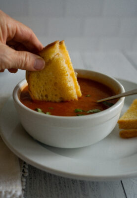 Slow Cooker Tomato Basil Soup in white bowl - dipping grilled cheese sandwich