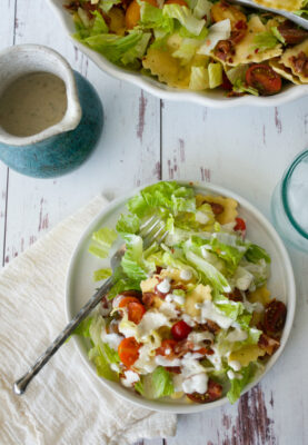 white salad plate with BLT salad and fork. Salad dressing in teal pitcher on the side.