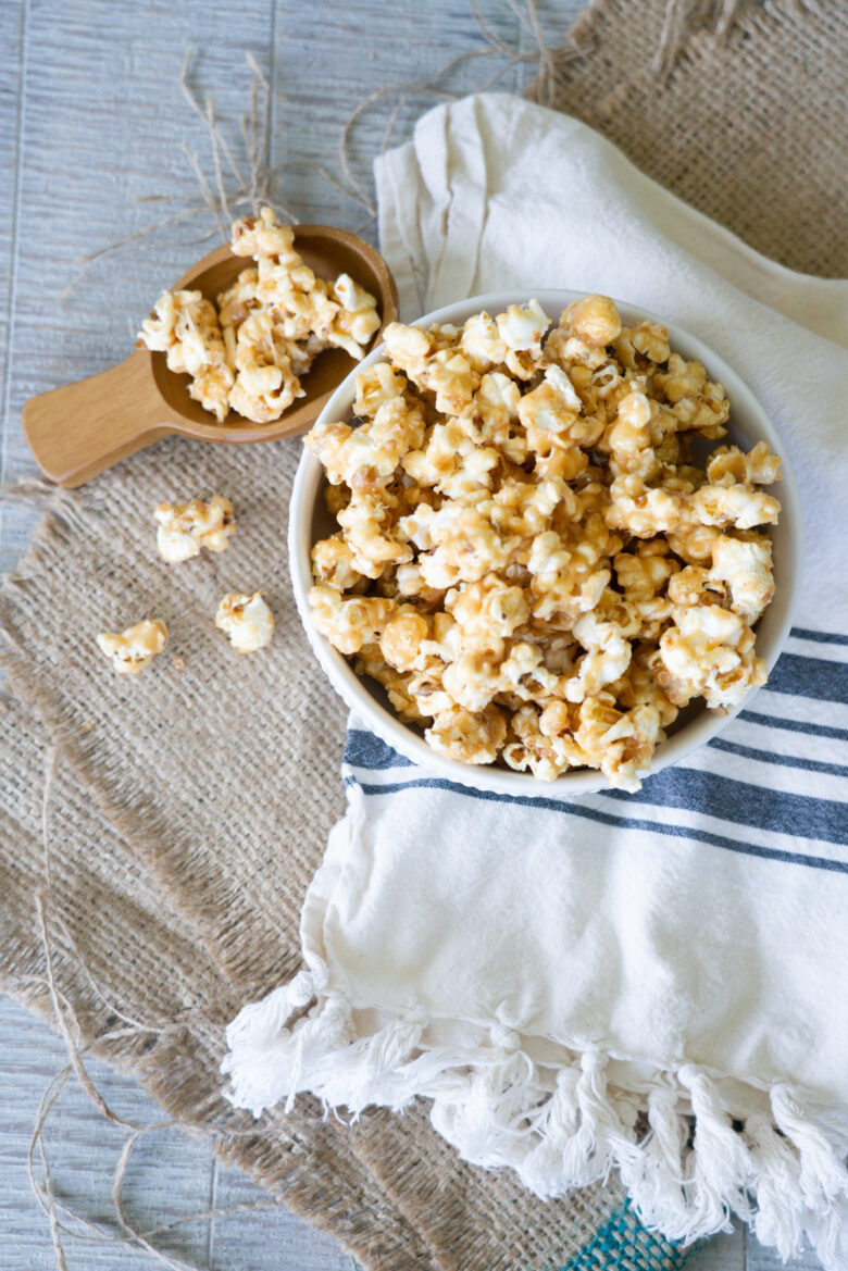 The Very Best Crunchy Caramel Corn in bowl with wooden scoop and burlap