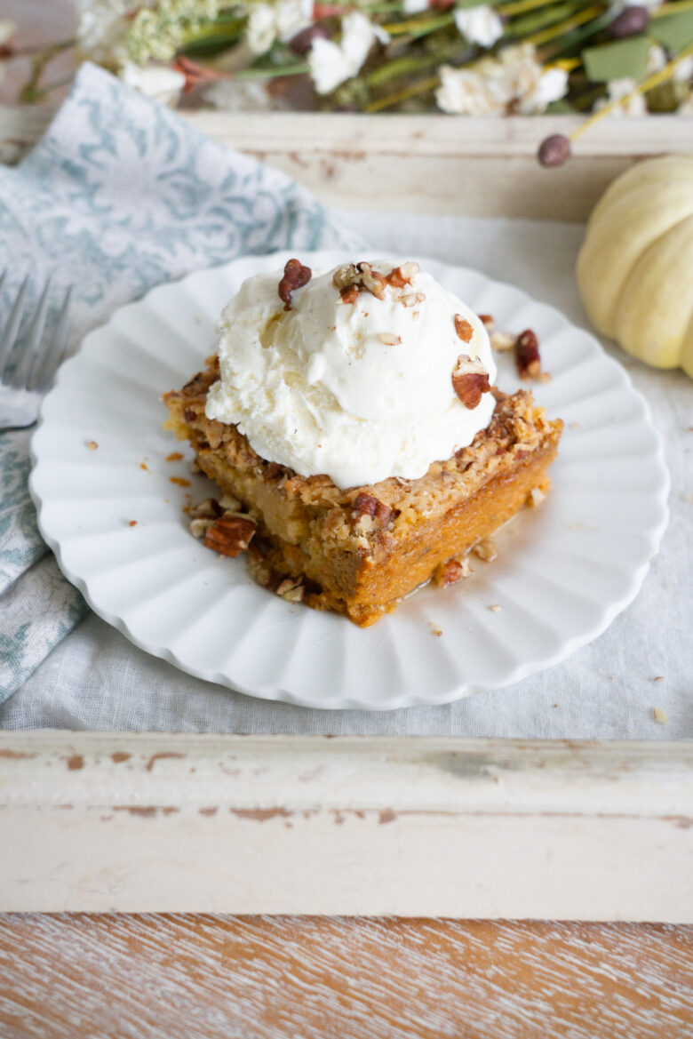 Pumpkin Dump Cake with vanilla ice cream and nuts on white plate. 