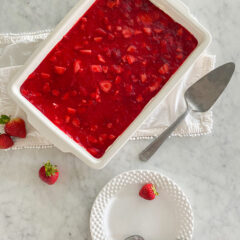 Strawberry Pretzel Jello Salad in white serving dish with serving plate and strawberries