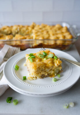 Closeup of Easy Tater Tot Casserole sprinkled with chopped green onions. Tater tot casserole in glass baking disnh in the background.