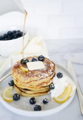 Lemon Ricotta Pancakes on white plate with syrup, whipped cream and berries.
