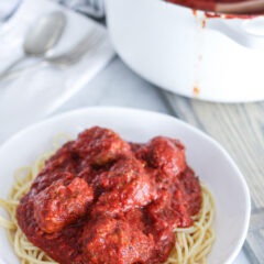 Close up of white bowl of spaghetti and meatballs. White pot of sauce in background.
