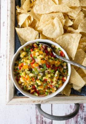Pinapple salsa in a bowl with tortilla chips on a tray.