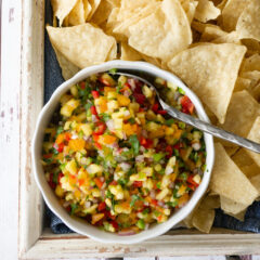 Pinapple salsa in a bowl with tortilla chips on a tray.